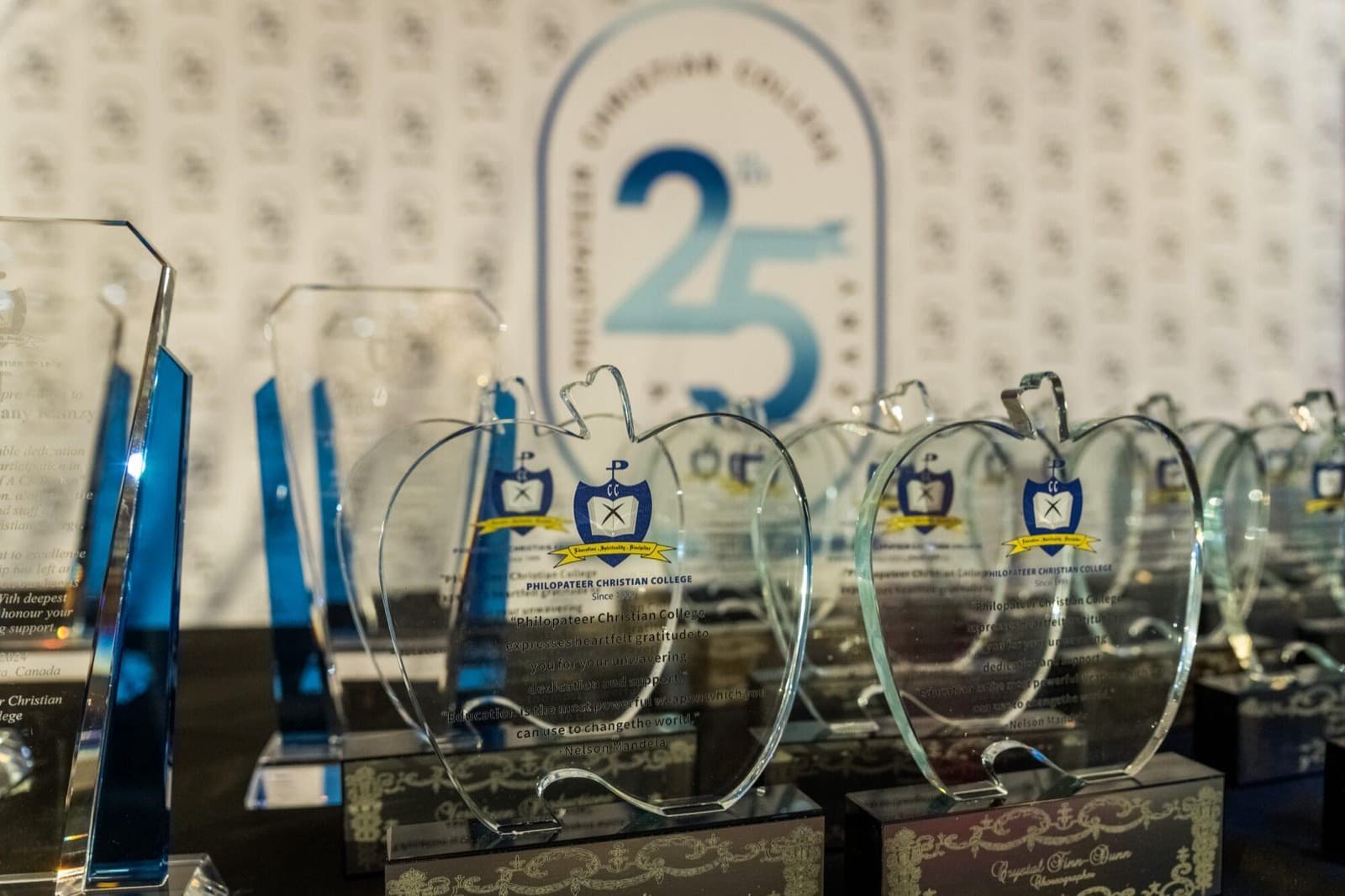 Glass apple-shaped trophies on a table in front of a backdrop with the school's 25th anniversary mark.